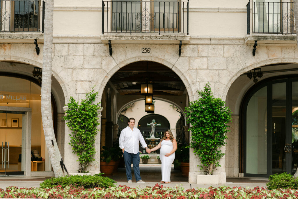Maternity photo in white dress walking through Worth Avenue archway