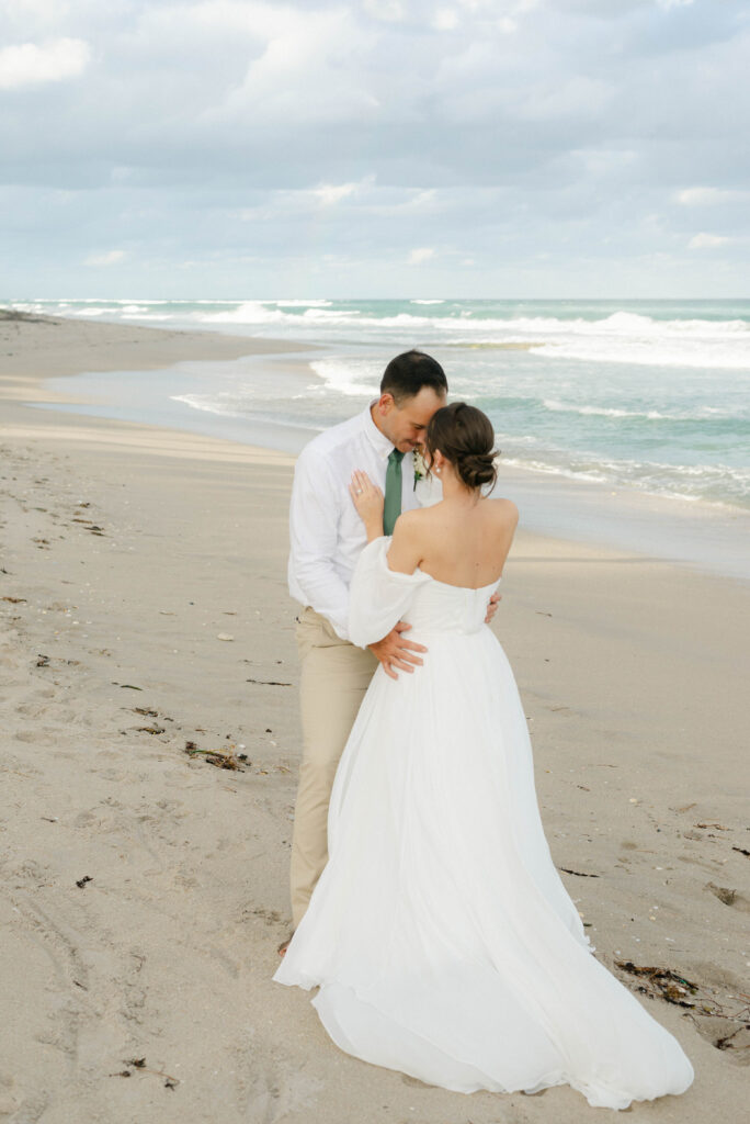 Groom hugging bride during golden hour on beach